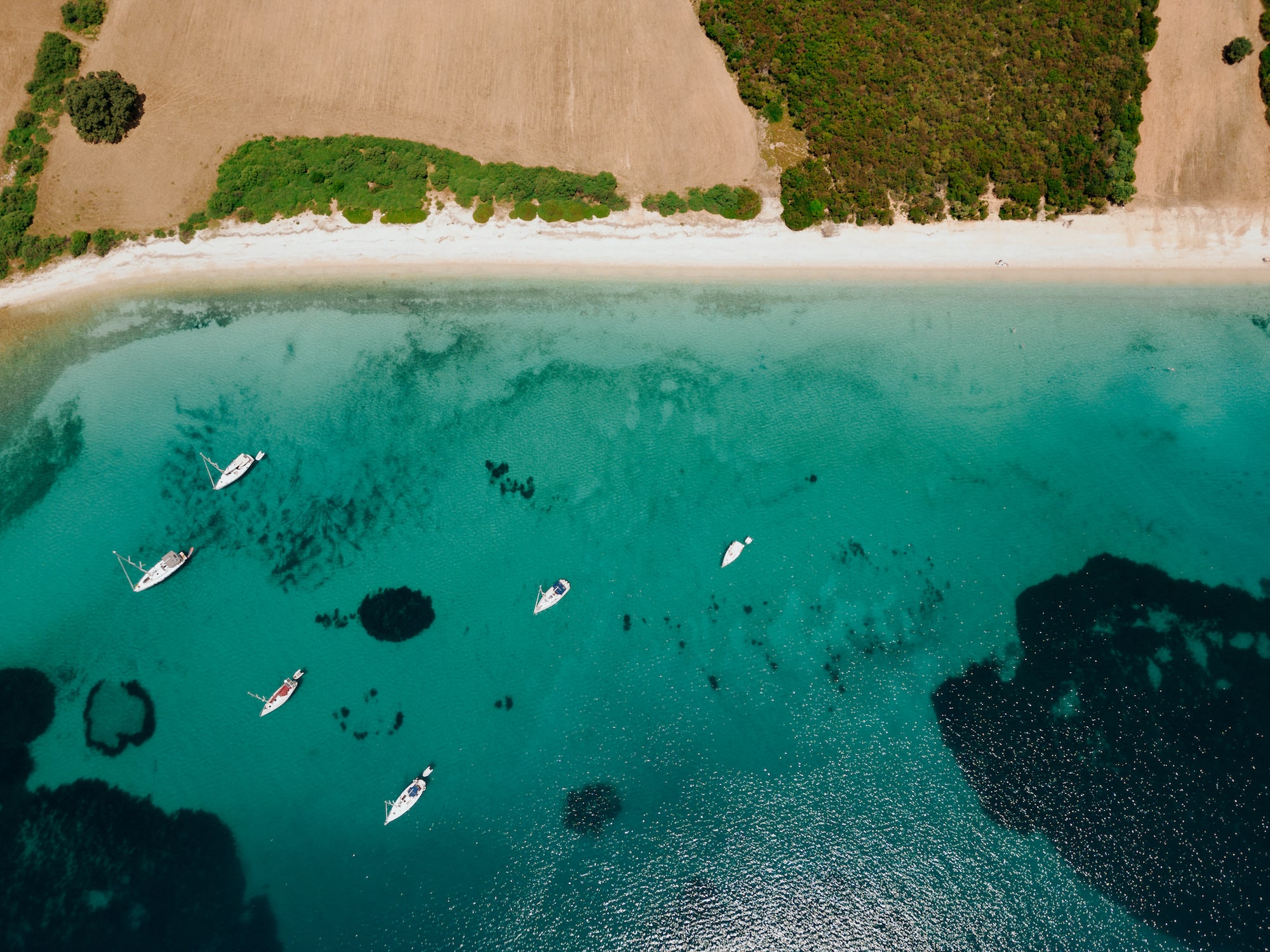 A drone image showing the beautiful Vathiavali Beach close to Paleros Greece. The image shows sailing boats and a stripe of sand with trees in the background